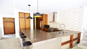A modern kitchen with a large island, wooden cabinets, and pendant lighting. - Casa Medina (Santa María Huatulco)