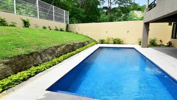 Una piscina rectangular con agua azul cristalina, rodeada por un borde de hormigón y un muro bajo de hormigón.