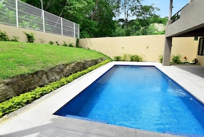 Una piscina rectangular con agua azul cristalina, rodeada por un borde de hormigón y un muro bajo de hormigón.