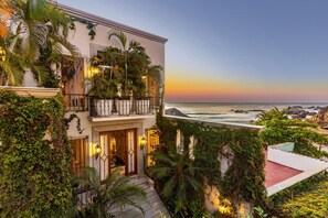A two-story building with a balcony overlooking the ocean, surrounded by lush greenery.
