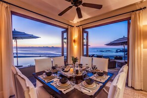 A dining table set for six with a view of the ocean at dusk.