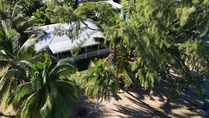 A building with a metal roof, surrounded by palm trees and other vegetation. - Beautiful house on white sand beach (Tahiti)