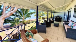 A covered outdoor area with wicker furniture, a view of palm trees, and a beach. - Beautiful house on white sand beach (Tahiti)
