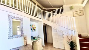 A staircase with white railings leading to an upper floor, a mirror with an ornate frame, a desk with a chair, and a potted plant. - Beautiful house on white sand beach (Tahiti)