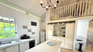 A modern kitchen with a central island, white cabinetry, a built-in oven, and a window overlooking greenery. - Beautiful house on white sand beach (Tahiti)