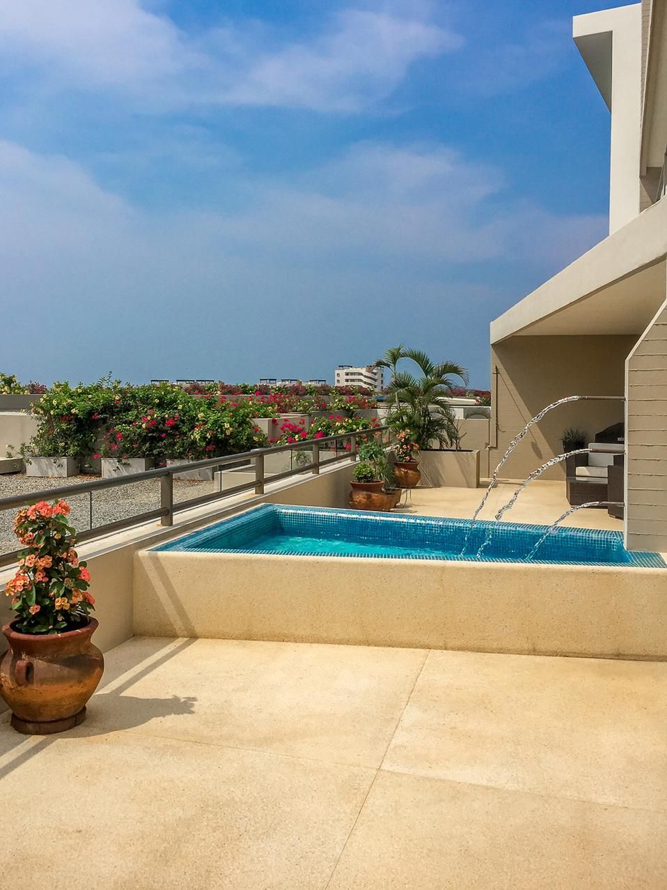 A rooftop pool with a clear view of the cityscape, surrounded by potted plants and a modern building structure.