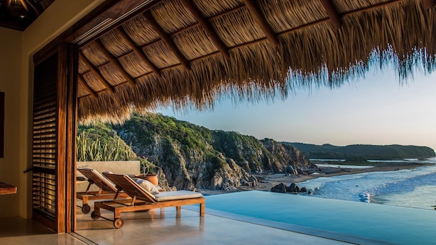 A modern infinity pool with a view of the beach and cliffs.