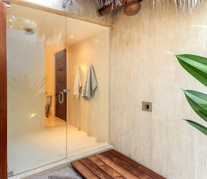 A modern bathroom with a glass shower enclosure, wooden bench, and a towel rack. - Villa Esquina del Cielo (Santa María Huatulco)