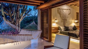 A bedroom with a bed, bedside tables, a chair, a small table, and a hammock.