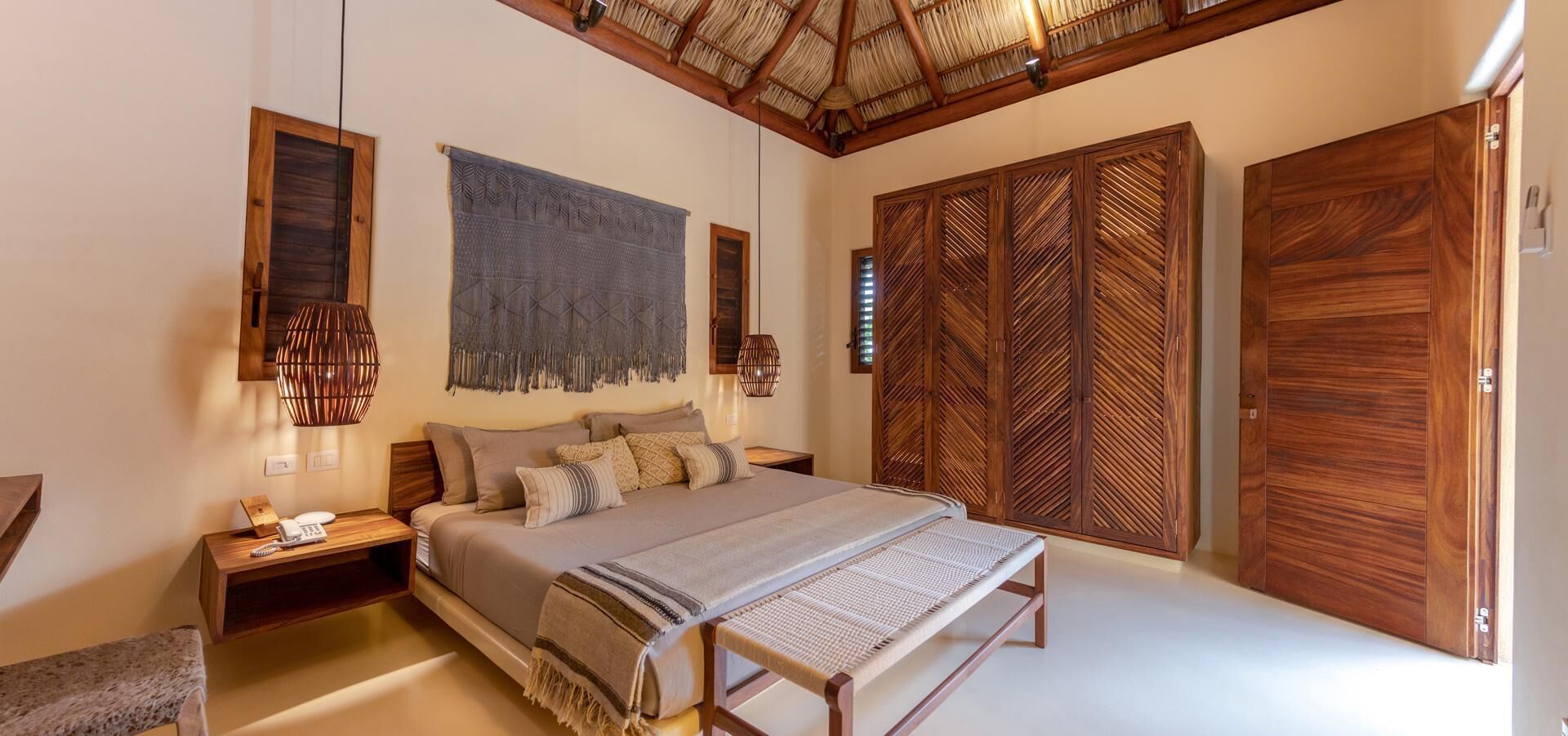 A bedroom with a large bed, wooden wardrobe, and a hanging light fixture.
