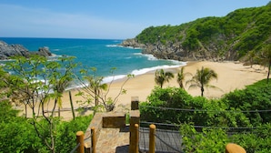 A coastal landscape with a beach, rocky cliffs, and lush greenery.