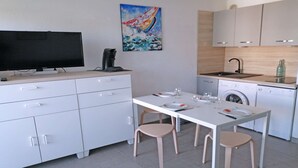 A modern kitchen with white cabinets, a dining table with chairs, a coffee maker, and a painting on the wall.