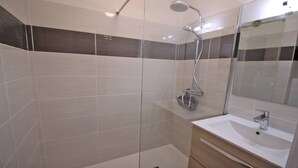 A modern bathroom with a glass shower enclosure, a white sink, and a mirror.