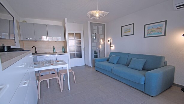 A modern kitchen with white cabinets, a dining table with chairs, a blue sofa, and two framed pictures on the wall.