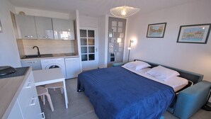 A compact hotel room with a bed, a desk, a washing machine, and a kitchenette.