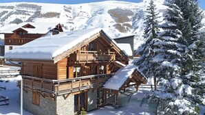 A wooden chalet with a balcony and a ski lift nearby, surrounded by snow-covered mountains.