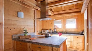 A wooden cabin kitchen with a granite countertop, wooden cabinets, a microwave, a coffee maker, and a window with a view of the forest.