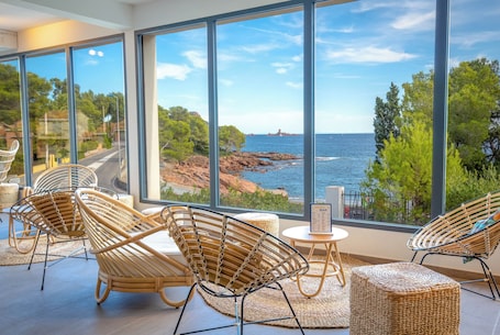 A room with large windows overlooking a coastal landscape, wicker furniture, and a small table with a menu.