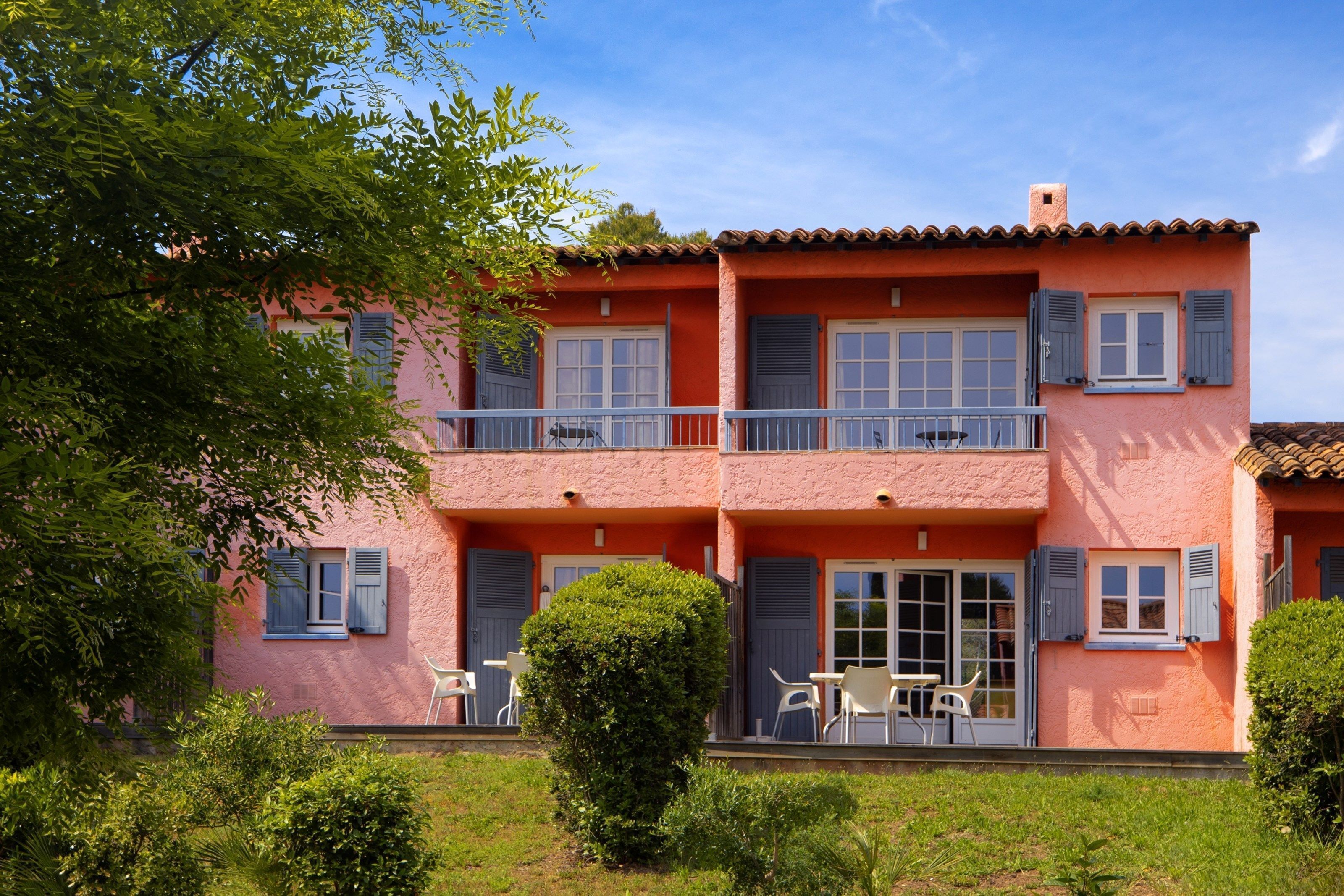 Een gebouw met twee verdiepingen, een balkon, witte tuinmeubels en een verzorgde tuin.