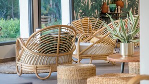 A room with wicker furniture, a rattan chair, a small table, and a potted plant. - Appart Abordable pour 4 | Accès Piscine (Saint-Raphaël)