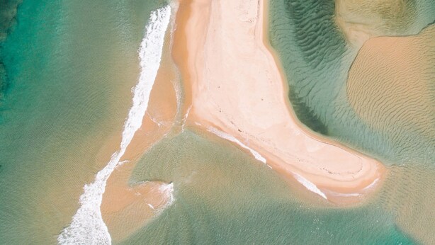 Eine Vogelperspektive zeigt einen Strand mit klarem Wasser und einer sandigen Küstenlinie.