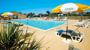 Ein Poolbereich mit Liegestühlen und Sonnenschirmen, ein Gebäude mit einer Beschilderung sowie ein klarer, blauer Himmel.