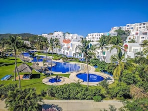 A resort with multiple swimming pools, palm trees, and white buildings with blue accents.
