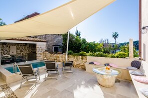 A stone building with a pool, outdoor seating, and a shaded area.