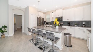 A modern kitchen with a central island, bar stools, stainless steel appliances, and a trash can. - SG2764 Storey lake  5 bed 5 bath Private Pool & Free Waterpark (Kissimmee)