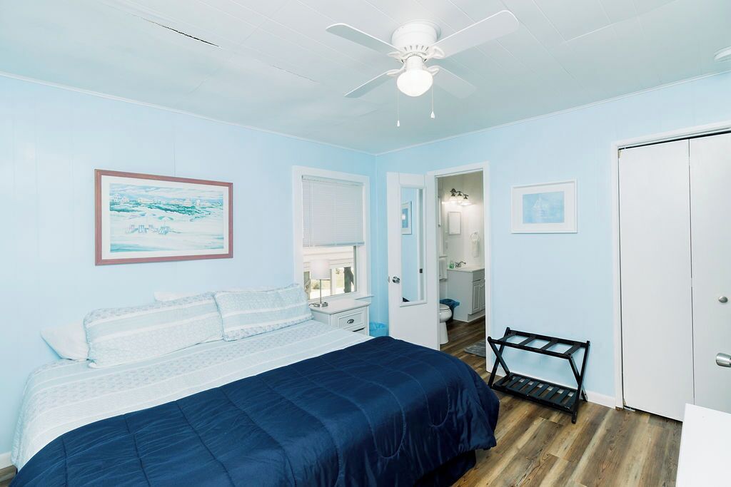 A bedroom with a bed, a ceiling fan, a door, and a small table.