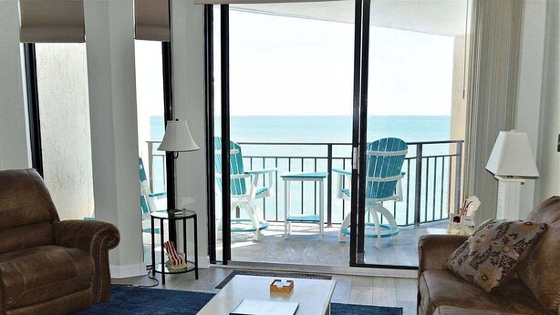 Ein Wohnzimmer mit einer großen Schiebeglasdoor zum Balkon mit Meerblick. Es gibt zwei Sofas, einen Couchtisch und eine Lampe.
