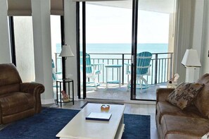 Ein Wohnzimmer mit einer großen Schiebeglasdoor zum Balkon mit Meerblick. Es gibt zwei Sofas, einen Couchtisch und eine Lampe.