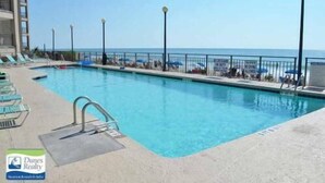 Ein Swimmingpool mit Blick auf den Ozean, umgeben von Liegestühlen und Sonnenschirmen.