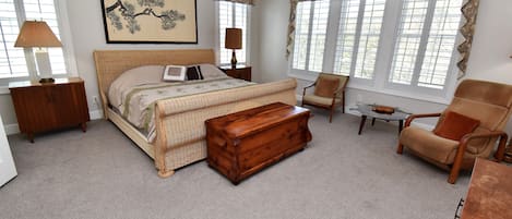 A bedroom with a large bed, a wooden chest, a chair, a small table, and a ceiling fan.