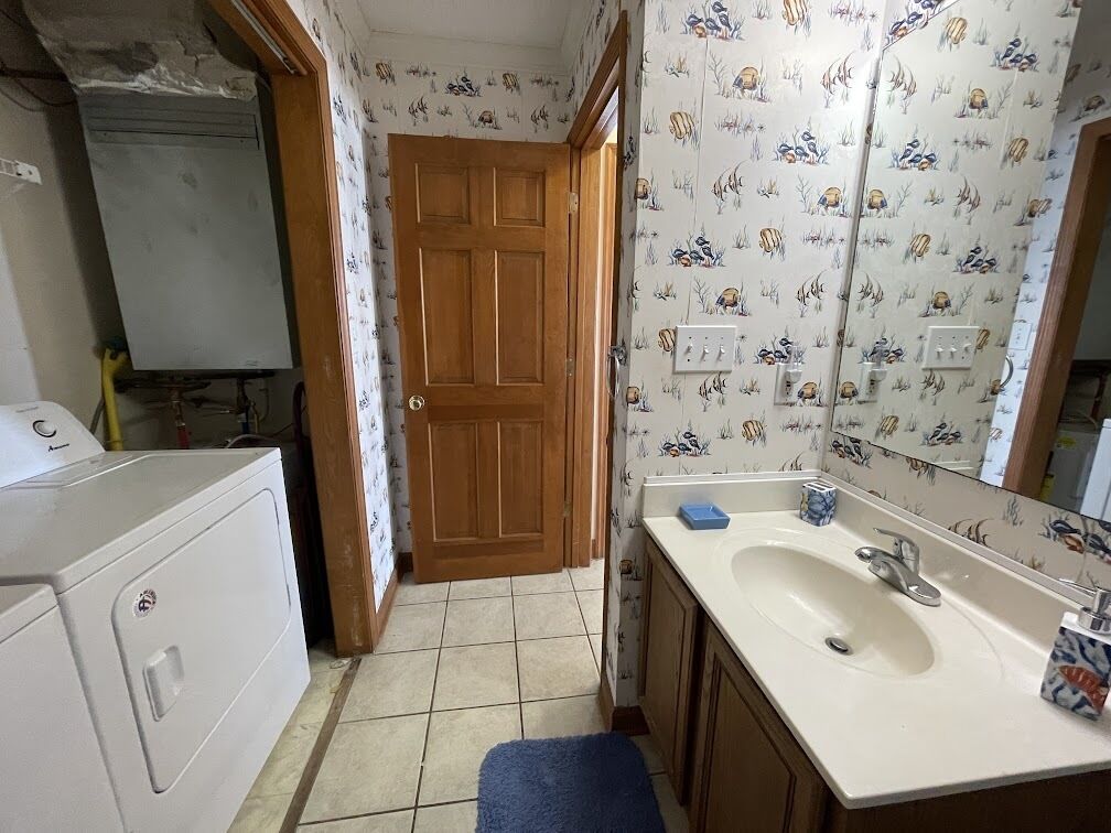 A small bathroom with a white sink, wooden cabinets, and patterned wallpaper.