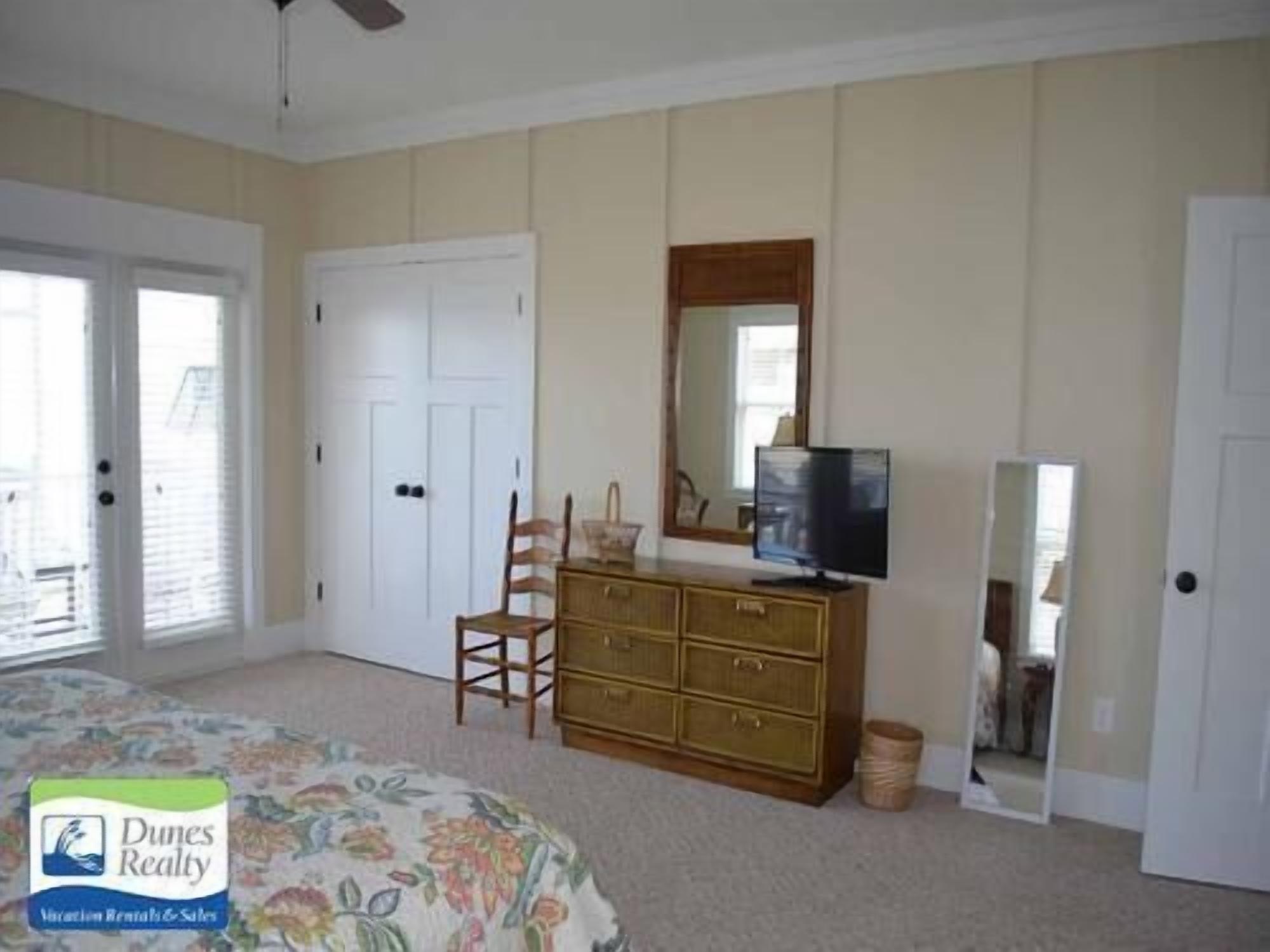 A bedroom with a bed, dresser, television, and a mirror.