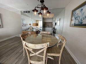 A dining area with a round wooden table and chairs, a chandelier, and a kitchen in the background.