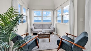 Ett rum med en soffa, två fåtöljer, ett soffbord och ett stort fönster med utsikt över havet.