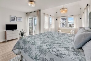 A bedroom with a large bed, a TV on a dresser, and a balcony with curtains. - House Call - Oceanfront in Garden City Beach (Garden City Beach)