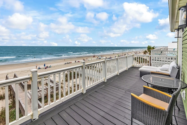 A wooden deck with outdoor seating overlooking a beach.