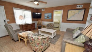 Una sala de estar con televisor, sofá, sillón, mesa de centro y lámpara.