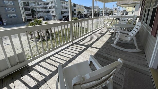 A covered outdoor area with a wooden deck, white chairs, and a table. - Electa's Place (Up) - Second Row in Garden City Beach (Garden City Beach)