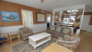 A living room with a sofa, armchair, coffee table, and a bookshelf. - Electa's Place - Second Row in Garden City Beach (Garden City Beach)