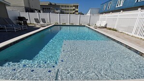 A rectangular swimming pool with clear water, surrounded by a white fence, and adjacent to a building with balconies. - Electa's Place - Second Row in Garden City Beach (Garden City Beach)
