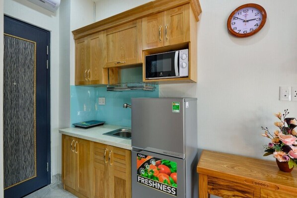 A kitchen with wooden cabinets, a microwave, a refrigerator, and a clock on the wall.