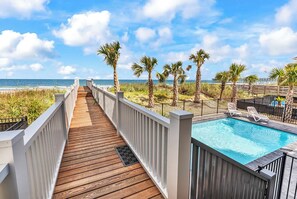 Eine Holzterrasse führt zu einem Pool mit Palmen und Blick auf den Strand.