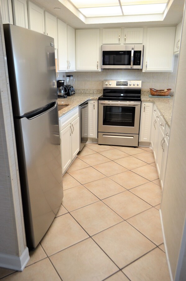 A kitchen with white cabinets, a stainless steel refrigerator, a microwave, an oven, and a coffee maker.