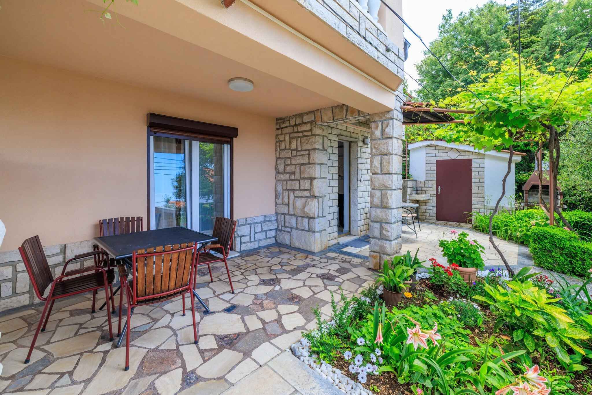 A patio with stone flooring, a table with chairs, and a small garden with various plants and flowers.