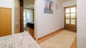 A hallway with a tiled floor, a wooden door, and a painting of sailboats on the wall. - Studio mit Terrasse und Klimaanlage (Jadranovo)