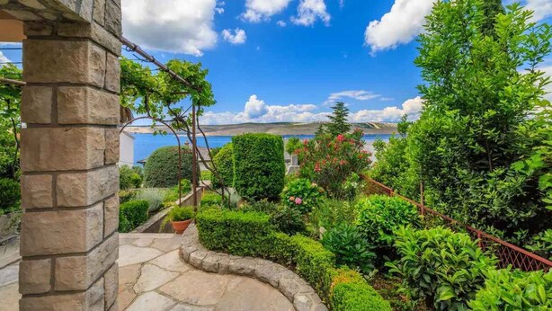 A stone pathway leading to a lush garden with various plants and a view of the sea. - Studio mit Terrasse und Klimaanlage (Jadranovo)